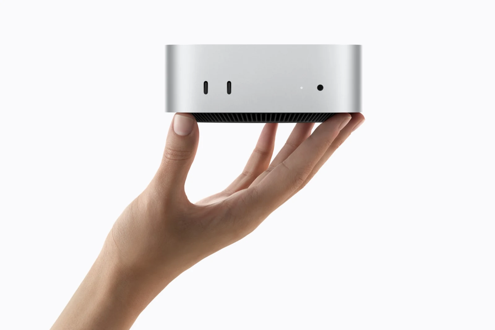Ruka drží stříbrný Mac mini, v popředí jsou přední porty