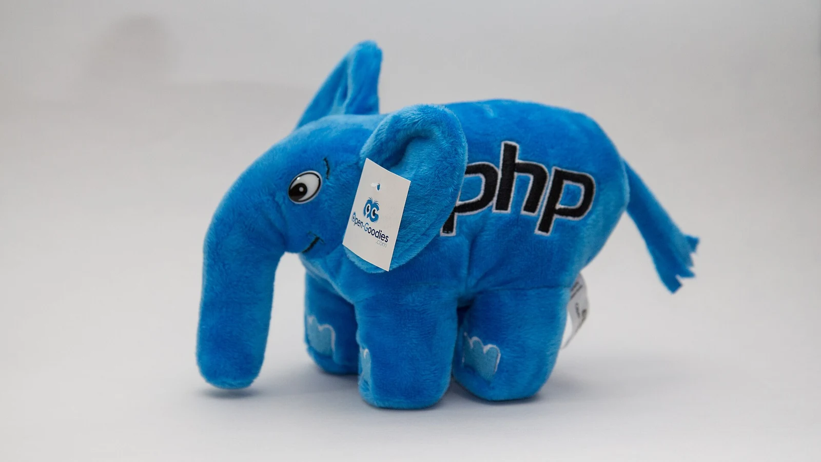Modrý plyšový slon elePHPant s vyšitým nápisem php na boku, maskot programovacího jazyka PHP, na světle šedém pozadí
