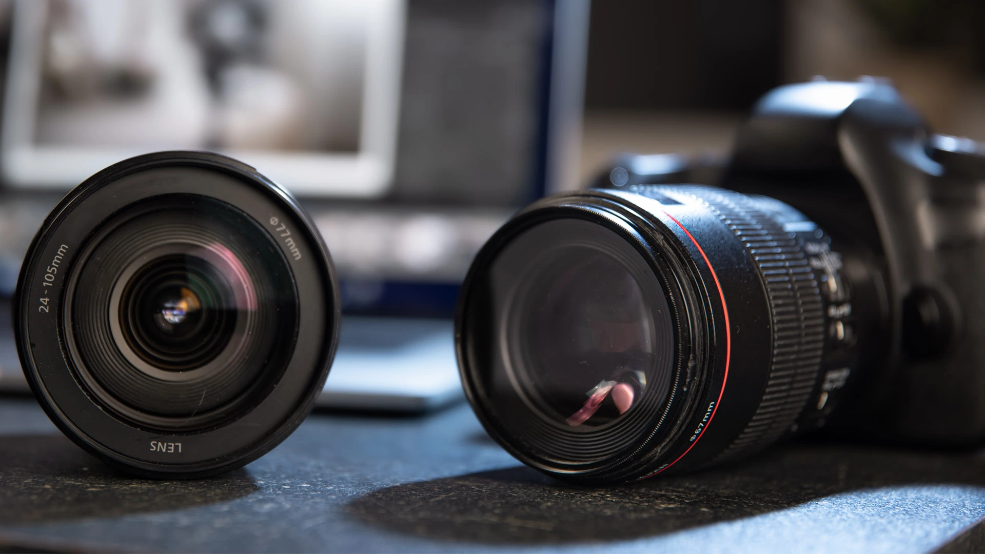 Dva fotografické objektivy a zrcadlovka položené na pracovním stole fotografky